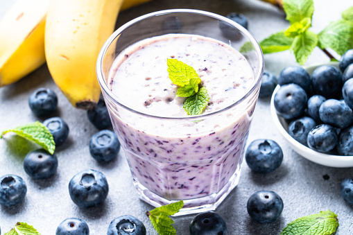 Blueberry banana smoothie or milkshake with fresh berries on stone table.