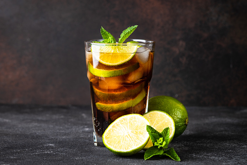 Cuba Libre alcoholic cocktail, iced drink on dark background.