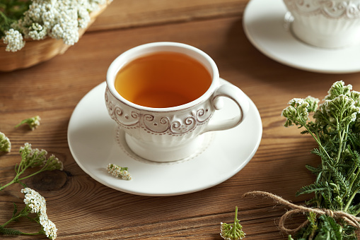 A cup of herbal tea with fresh yarrow flowers on a wooden table
