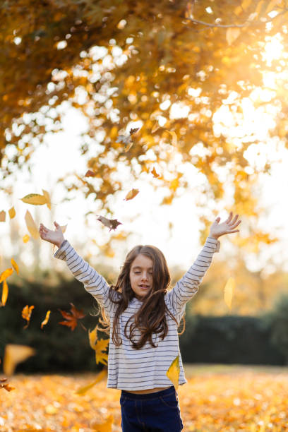 istock Playful girl cheering and throwing dry maple leafs in the park 1632273568