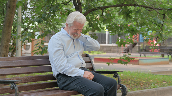 Tired Senior Old Man Sitting Outdoor with Neck Pain
