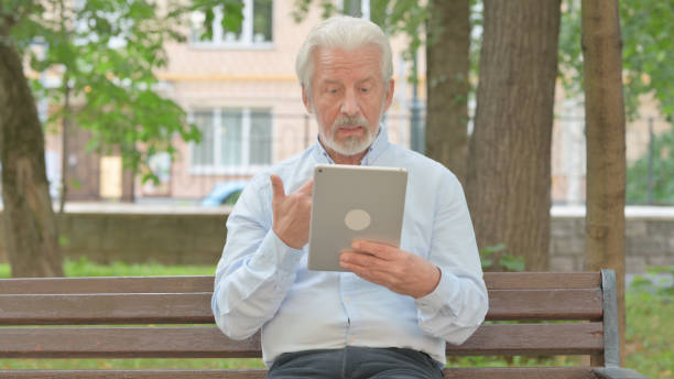 istock Senior Old Man Doing Video Chat on Tablet while Sitting in Park 1632300658