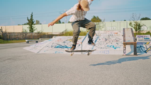 SLO MO Teenage Boy Performing Kickflip with Skateboard in Skate Park on Summer Day