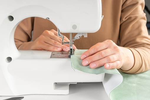 istock Tailor hands stitching green fabric on modern sewing machine at workplace in atelier 1632312171