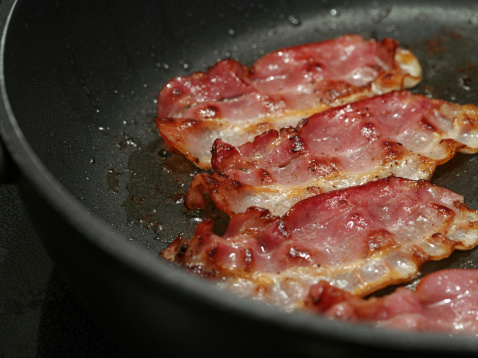 Macro photo of bacon being fried in a pan.