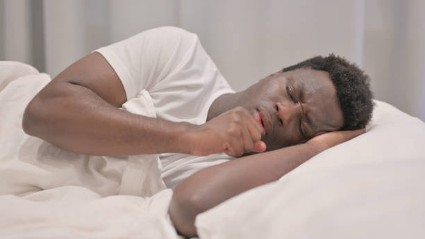 istock Coughing African American Man Lying in Bed on Side 1632318020