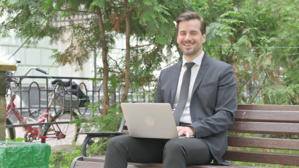 istock Middle Aged Businessman Smiling at Camera while Working on Laptop Outdoor 1632319592