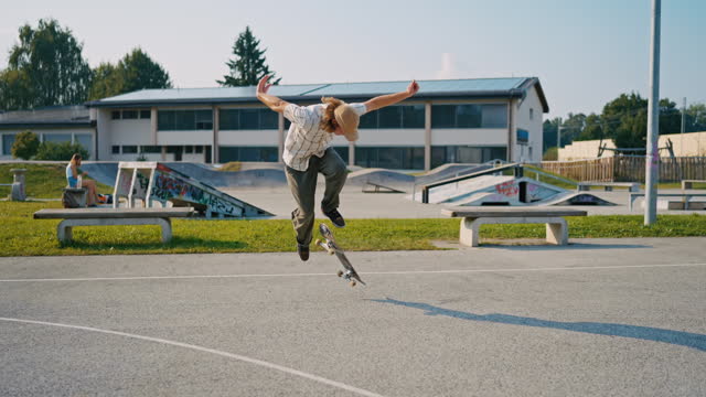 SLO MO Hipster Boy Performs Kickflip with Skateboard in Skate Park on Sunny Day