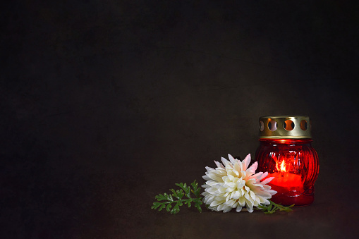 Grave candle lantern and flower on dark grunge background with copy space