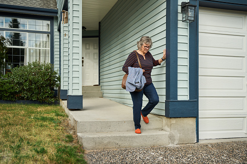 Mature woman carefully walking down her porch steps at home and grimacing from knee pain