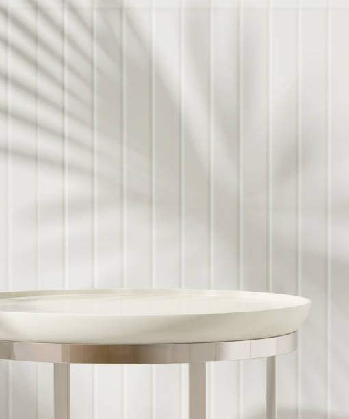 istock Clean white round table podium with chrome steel leg in sunlight with palm leaf shadow on wainscot wall 1632392272