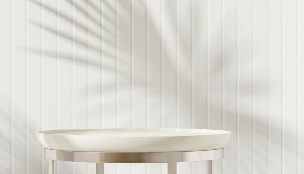 istock Clean white round table podium with chrome steel leg in sunlight with palm leaf shadow on wainscot wall 1632393322