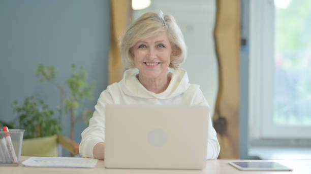 istock Senior Old Woman Smiling at Camera while Working on Laptop 1632405319