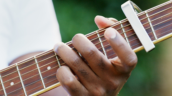 Close-up of man's fingers on fretboard while playing acoustic guitar