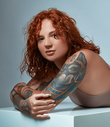 Portrait of a tattooed young woman with copper-colored hair.  Skin retouched and clean photograph.