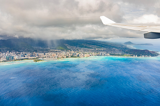 View from plane overlooking Honolulu city in Oahu, Hawaii on a bright sunny day with turquoise blue ocean.