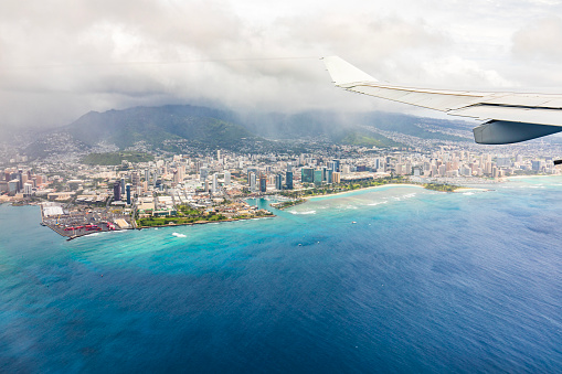 View from plane overlooking Honolulu city in Oahu, Hawaii on a bright sunny day with turquoise blue ocean.