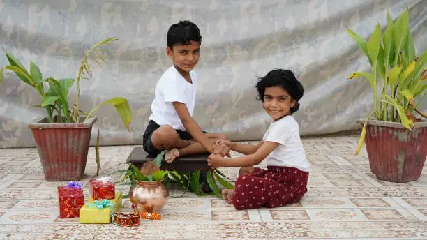 Photo of little Indian Sister tying Rakhi to Her little brother's wrist and exchanging gifts and sweets on Raksha Bandhan or Bhai Dooj festival