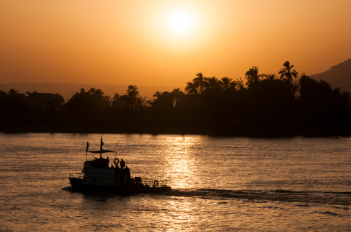 Silhouette of a police boat, machine gun mounted on the front, motoring up the Nile River at sunset in Luxor, Egypt