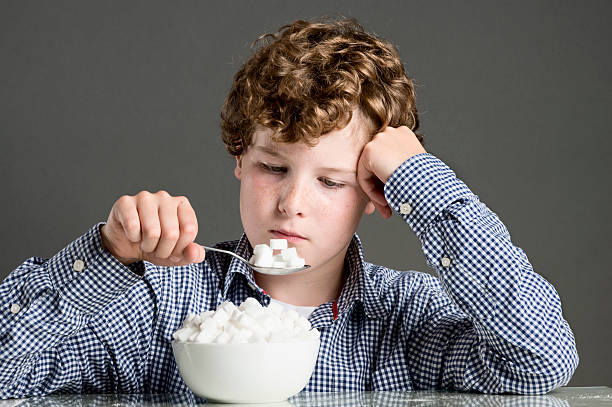 Child Eating Too Much Sugar Concept Young boy 10 years old pouring out some sugar cubes into a bowl to illustrate the idea of too much sugar in our diet.Young boy 10 years old building a pyramid out of sugar cubes to illustrate the idea of too much sugar in our diet. boys bowl haircut stock pictures, royalty-free photos & images