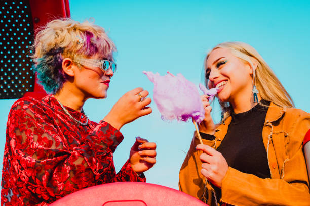 istock Female friends smiling while enjoying eating cotton candy together. 1632589165