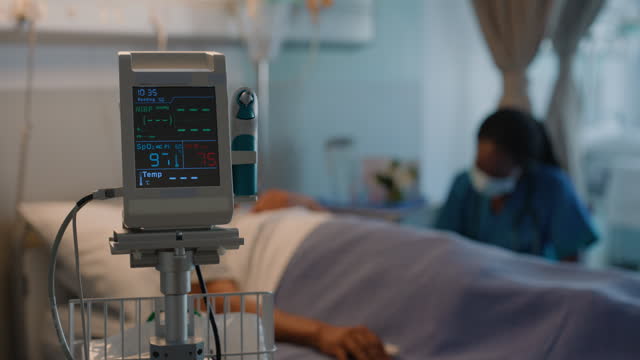Healthcare, vital machine and doctor with a man in a bed while sick after surgery. Bokeh, cardiology and senior patient speaking to a black woman or nurse for notes, service and hospital consultation