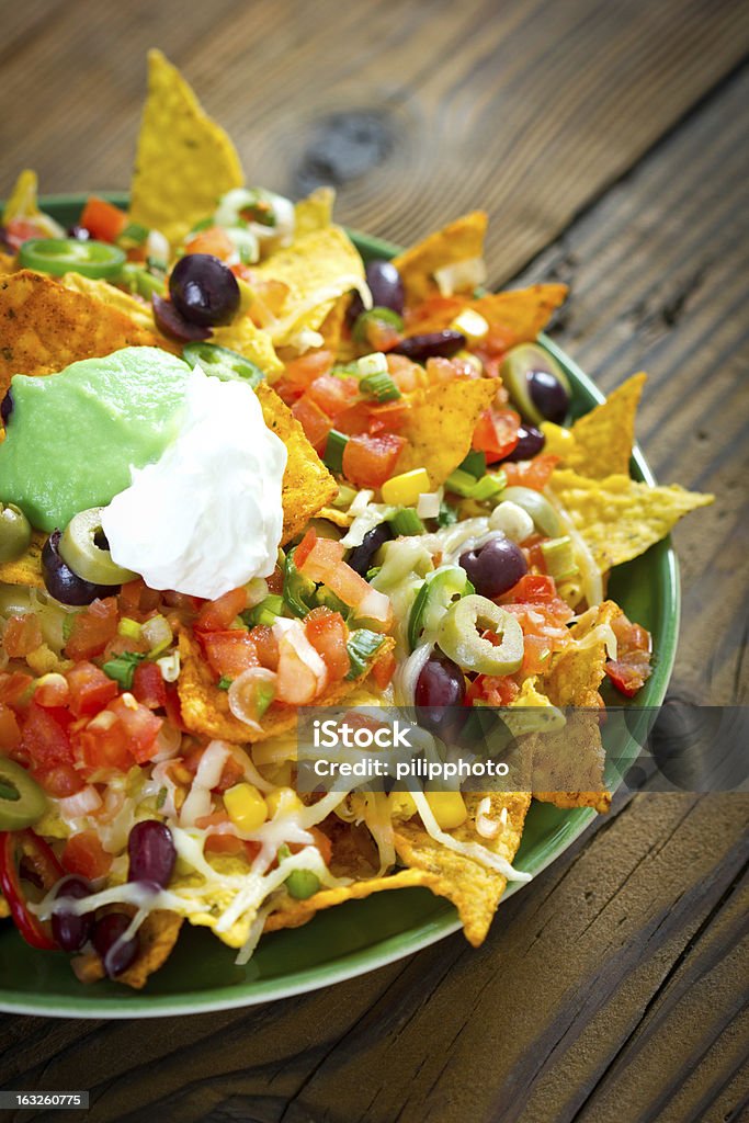 Fully loaded nachos in a green plate on a wooden table Nachos on the plate Nacho Chip Stock Photo