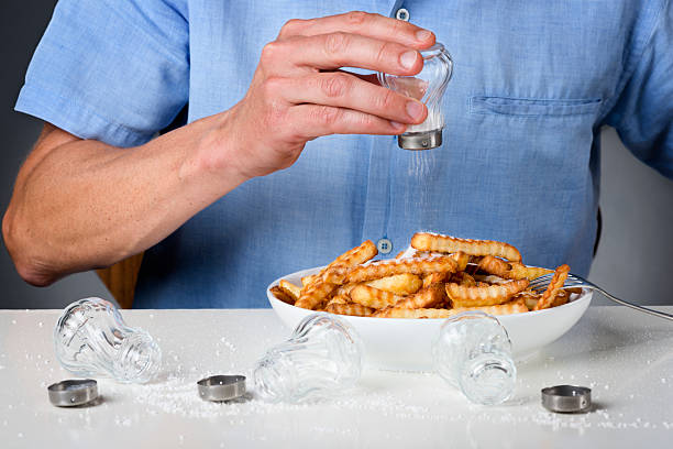 Too Much Salt Adult man putting too much salt on his bowl of chips. salt seasoning stock pictures, royalty-free photos & images