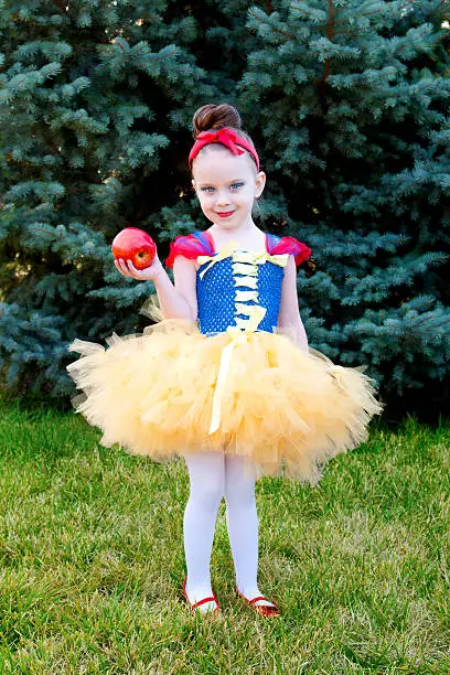 Little girl dressed as Snow White with an apple, outdoors.