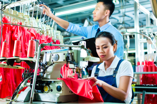 Seamstress or worker in a factory sewing with a sewing machine, a foreman checks the yarn