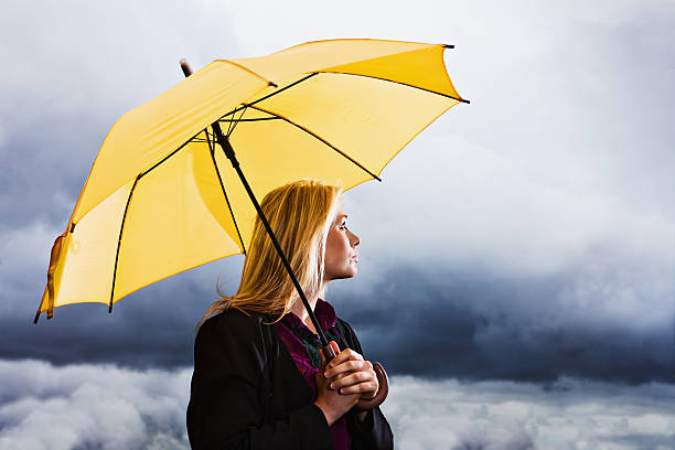 ストーミー悪天候： wistful ブロンドにイエローの傘ウェイツ出力雷雨 - umbrella women storm yellow ストックフォトと画像