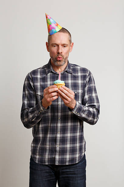 Homme au Chapeau de fête soufflant Bougie sur Cupcake - Photo