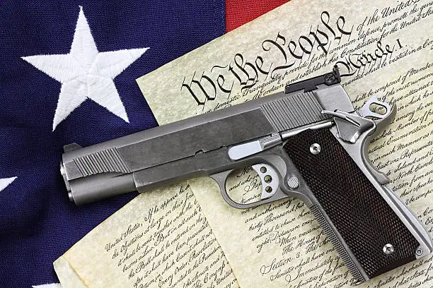 Handgun lying over a copy of the United States constitution and the American flag.