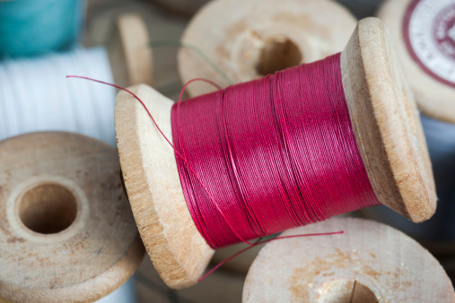 Macro close-up of red sewing thread on a vintage wooden spool among other spools in different sizes and colors found in an old Dutch wooden sewing box, shallow DOF.