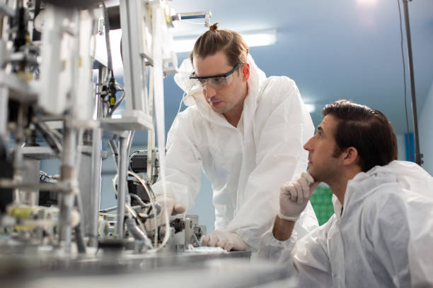 istock Machine staff, mask production department. Engineer wearing protective suit Inspecting quality of masks. machine production manufacturing factory. 1632749972