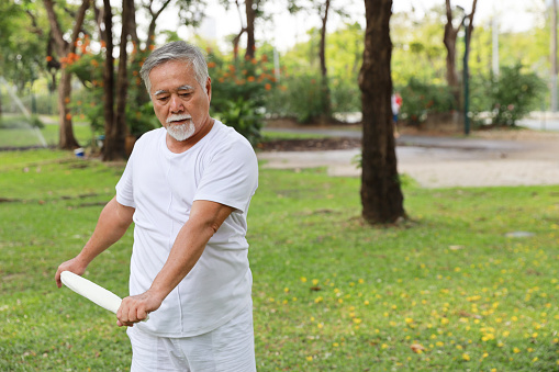 Asian senior man practice yoga excercise, tai chi tranining, stretching and meditation together with towel for relax healthy in park outdoor after retirement. Happy elderly outdoor lifestyle concept