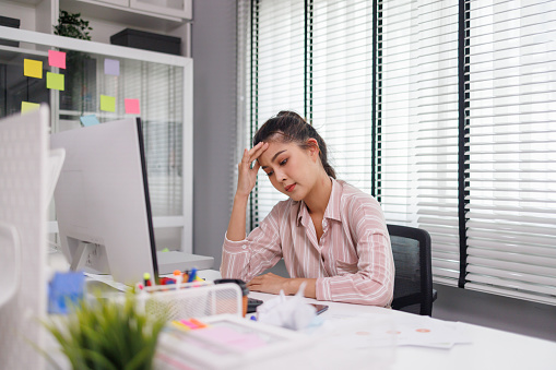 Asian woman is stressed while working in office, Tired asian businesswoman with headache at office, feeling sick at work.