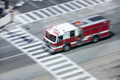 An overhead motion panned view of a fire engine racing to the scene of an emergency on a city street.