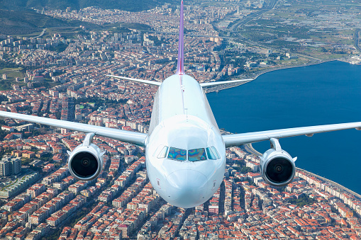 White passenger airplane flying over modern Izmir city