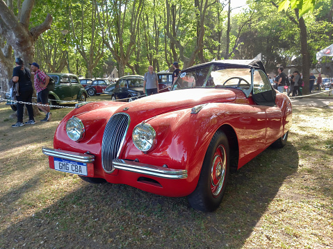 San Isidro, Argentina - Oct 7, 2022: Old red sport 1953 Jaguar XK 120 roadster in a park. Nature, trees. Autoclasica 2022 classic car show.