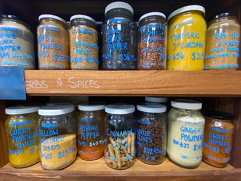 Spices Set in Mini Bottles, such as basil, turmeric, salts, chilli flakes, cumin seeds on dark wooden background