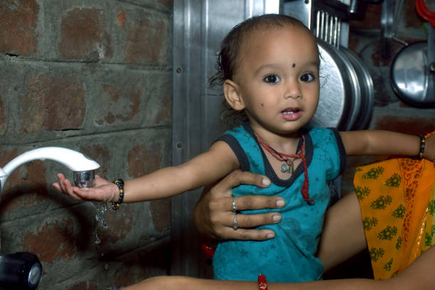 little cute girl playing with her mother with tap water, kitchen background, rural setting
