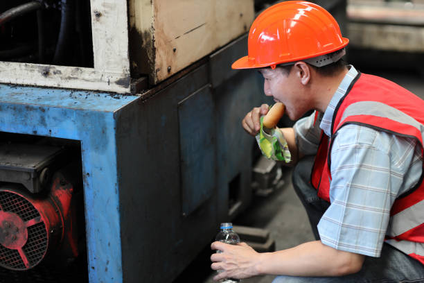 Asian technician engineer or worker man in protective uniform having lunch and eating sandwich and water at industry manufacturing factory