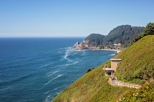 A pathway to sea lion caves against the cliff in the foreground, and the Heceta Head lighthouse in the background.
