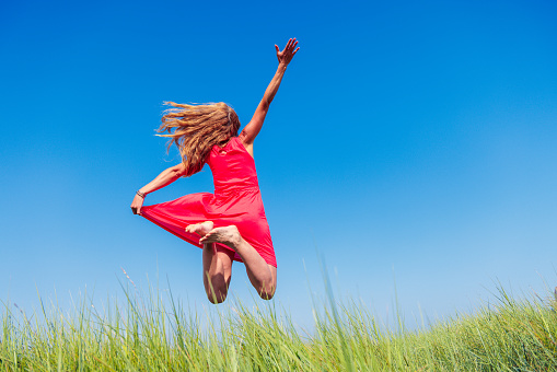 Happy woman in red dress jumping on blue sky and green grass- relaxing, active, fun,freedom,wellness concept