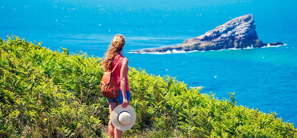 Woman with backpack and hat looking at island in atlantic ocean- Adventure, travel, vacation concept
