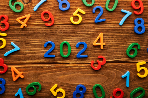 The concept of changing 2023 to 2024 made up of colorful numbers on a wooden background.