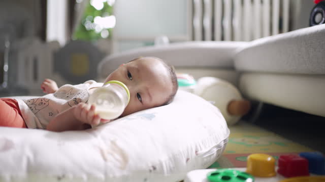 Baby Boy Bottle Feeding by Himself on Babybed at Home