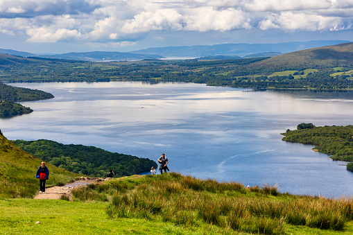 Hikers and walkers descending Conic Hill overlooking Balmaha and Loch Lomond in the Scottish Highlands.