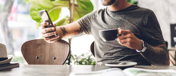 istock Handsome hipster man relaxing using digital smartphone with coffee and looking at screen typing message at table in cafe and restaurant,playing game online and social media 1632915198